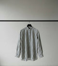 A long-sleeve button-up shirt with vertical black and white stripes, shown hanging against a dark red background.