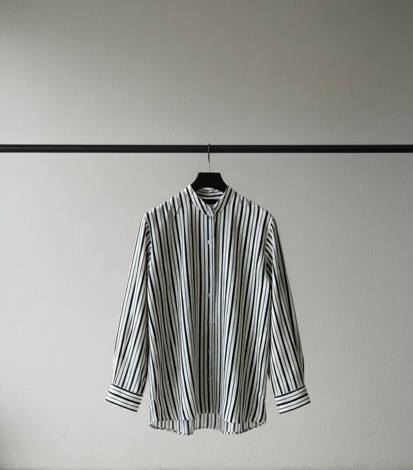 A long-sleeve button-up shirt with vertical black and white stripes, shown hanging against a dark red background.