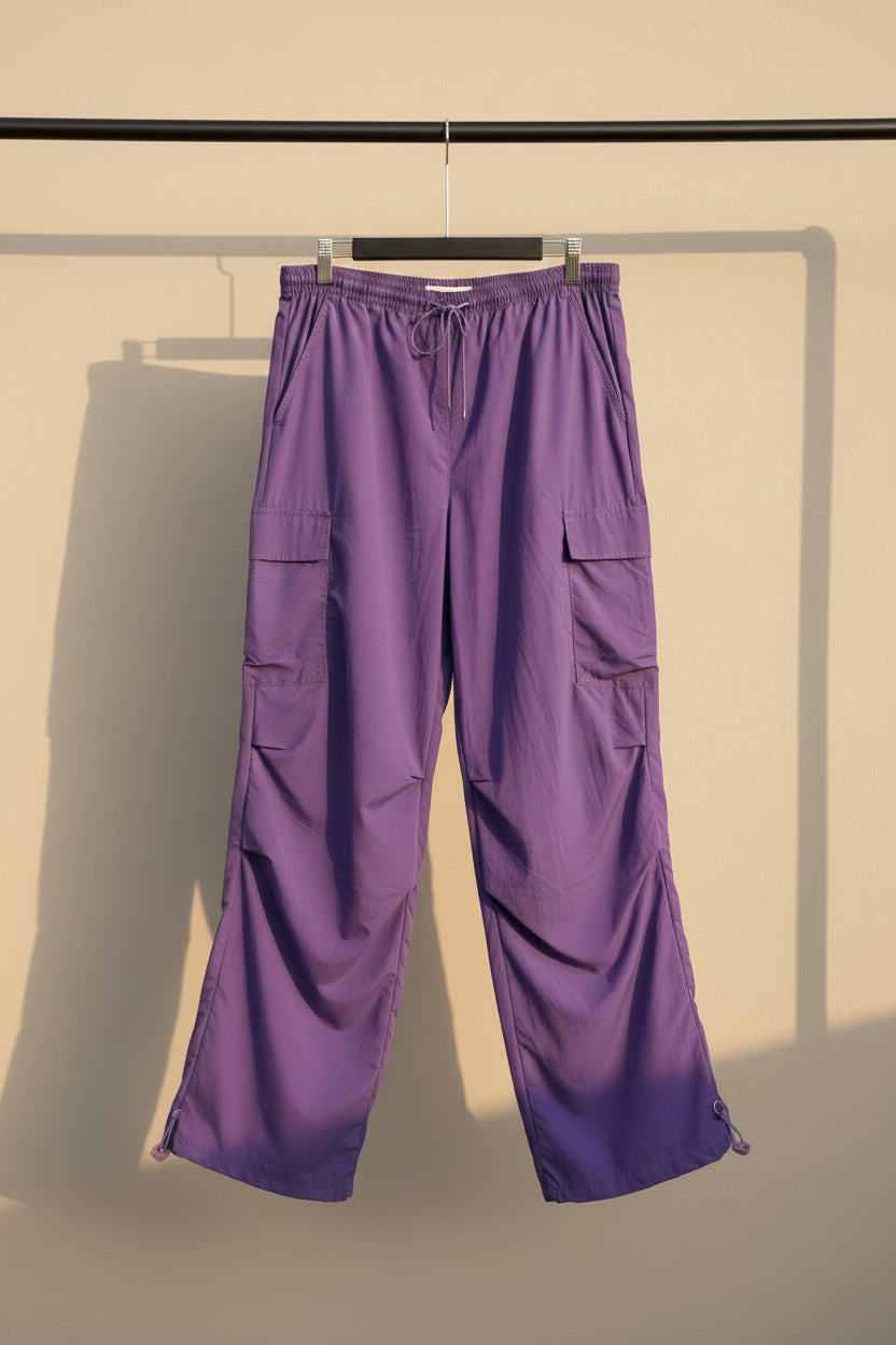 Purple cargo pants with an elastic drawstring waist and multiple utility pockets, hanging against a gray fabric backdrop.