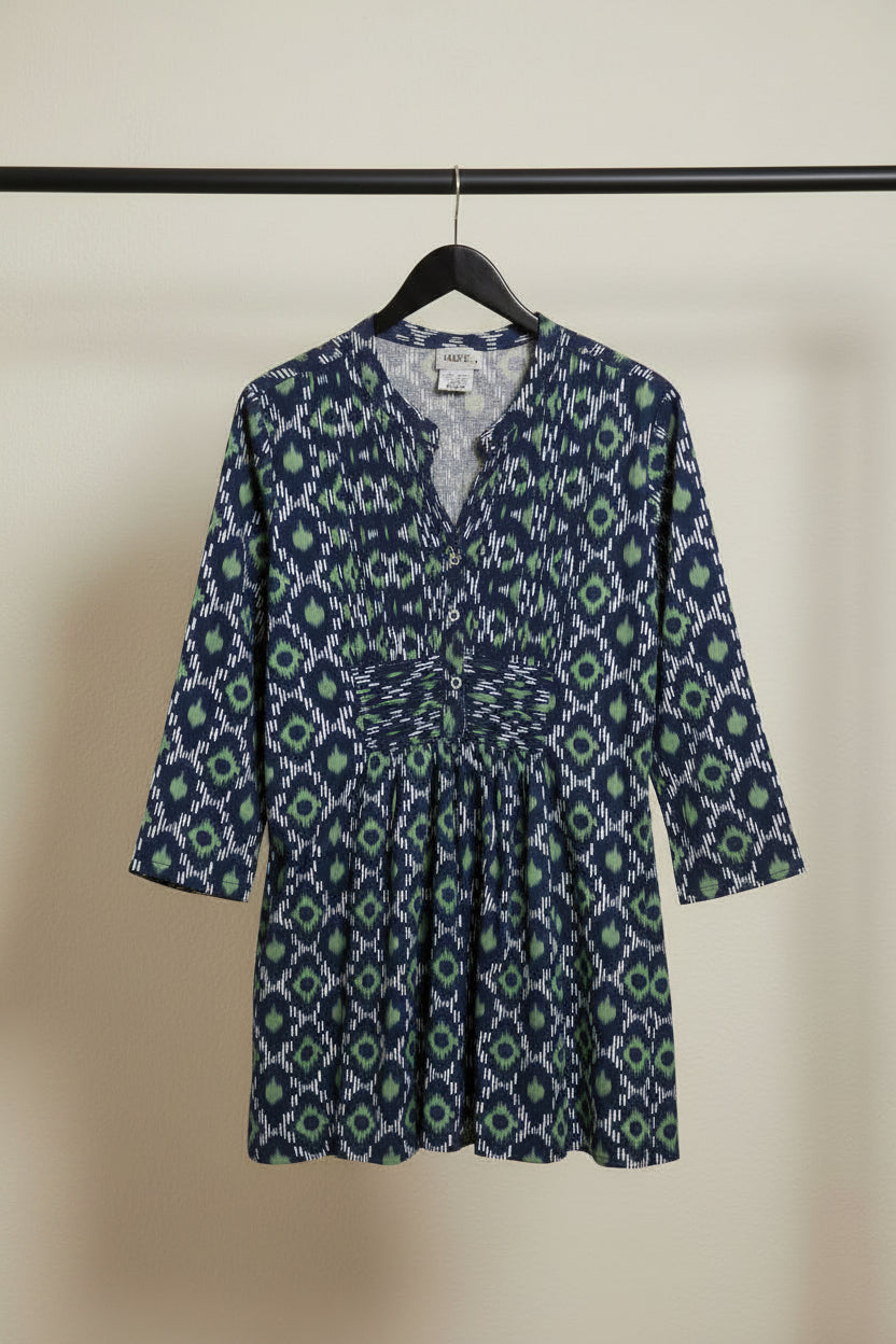 A women's long-sleeve tunic dress with a navy blue, green, and white ikat geometric pattern, featuring a button-up front and a matching fabric tie belt at the waist.
