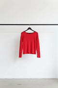 A bright red long-sleeve knit top with a fuzzy, textured fabric and a wide boat neckline, hanging on a wooden hanger against a white fabric backdrop.