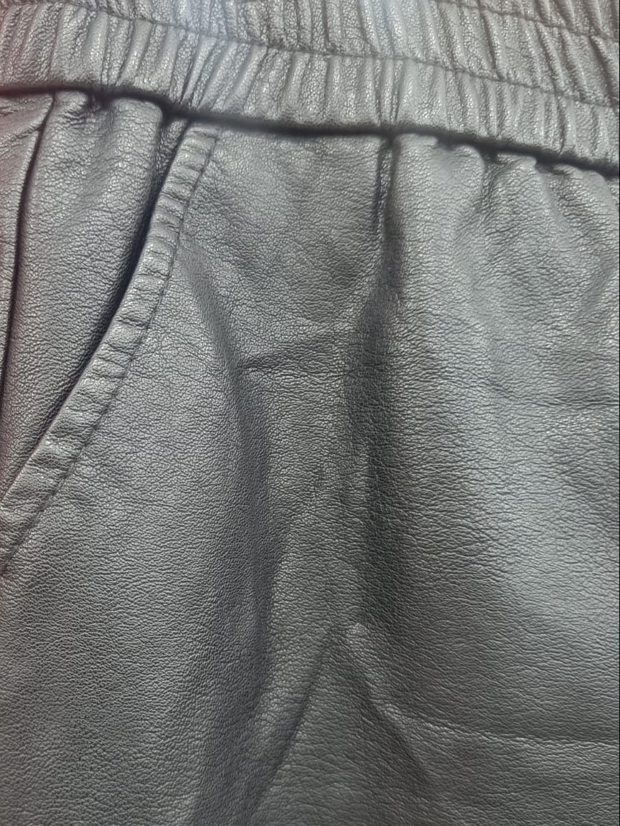 Close-up of dark gray faux-leather trousers with an elastic waistband, laid flat against a red background.