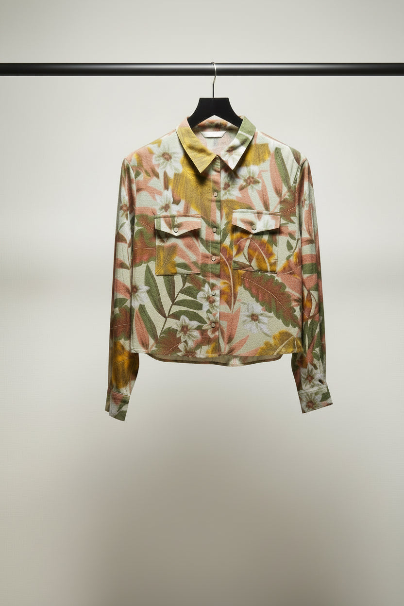 A long-sleeve button-up shirt with a tropical floral and leaf print in green, orange, brown, and white, laid flat on a light gray background.