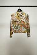 A long-sleeve button-up shirt with a tropical floral and leaf print in green, orange, brown, and white, laid flat on a light gray background.