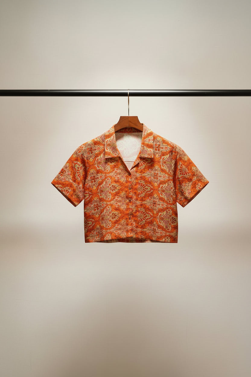 A short-sleeve button-up shirt with a red and beige damask pattern, laid flat on a white fabric background.
