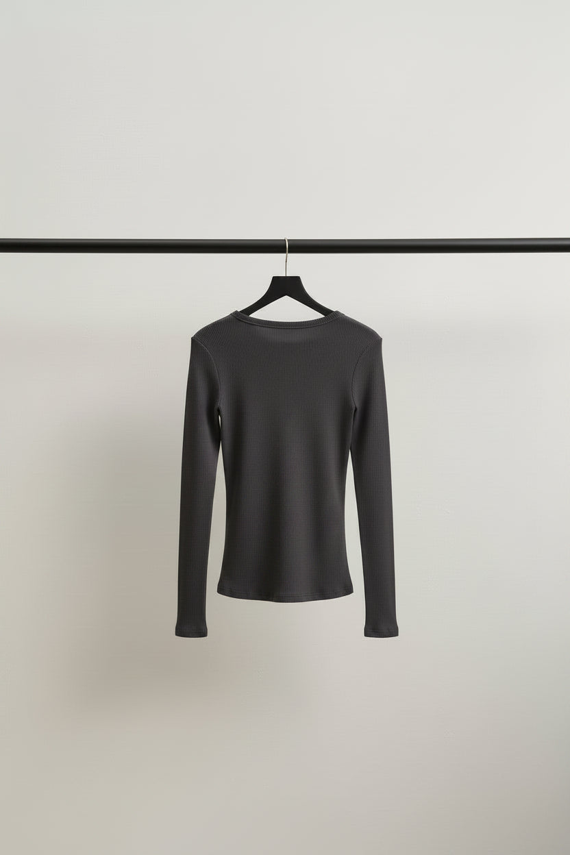 A dark brown long-sleeve knit top hanging outdoors on tree branches with green leaves and a light-colored wall in the background.